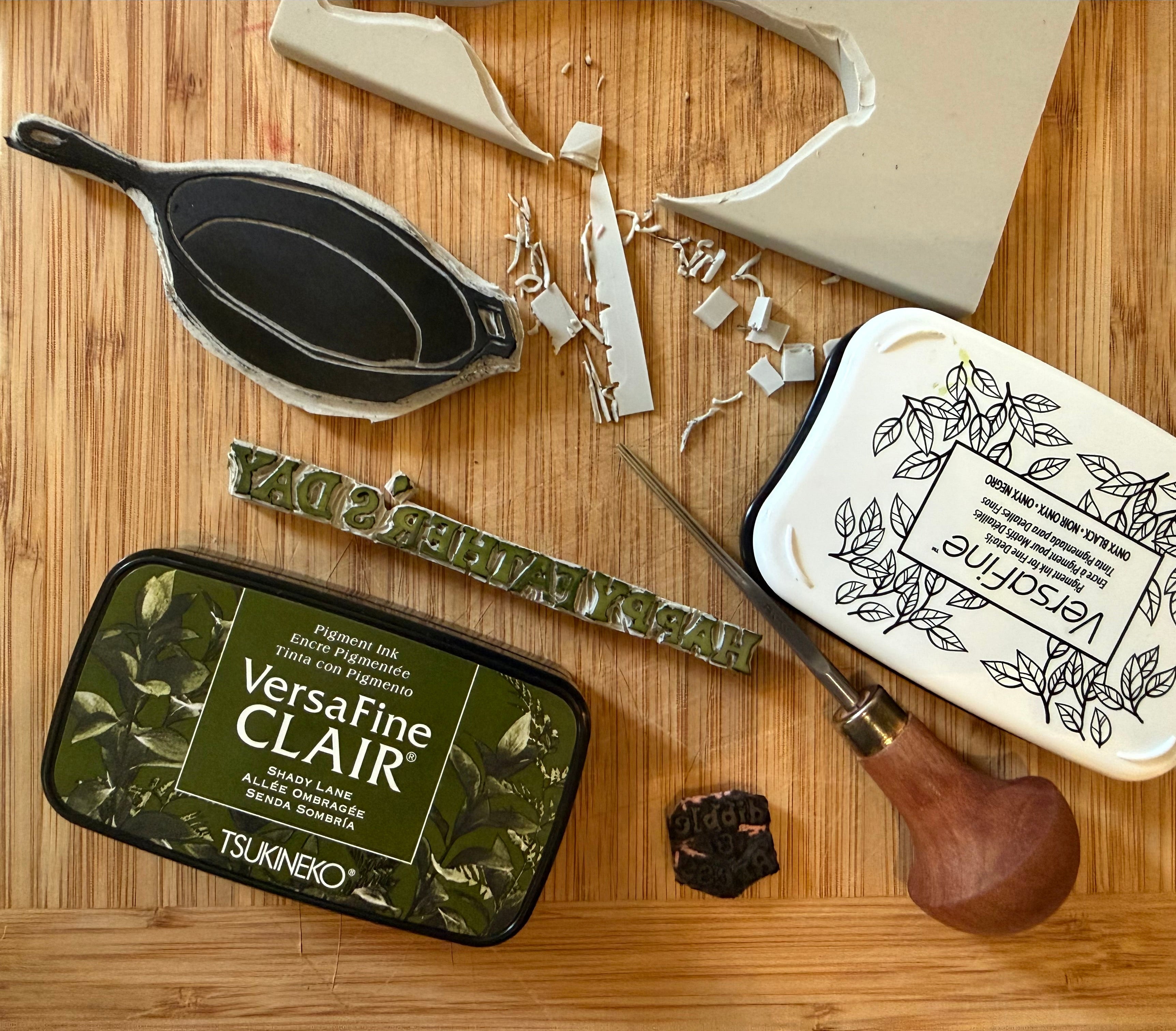 Hand carved linocut stamps, chisel carving tool and ink pads on a wooden surface